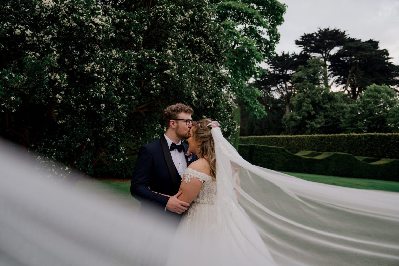 bride and groom in an embrace with long veil blowing in the wind